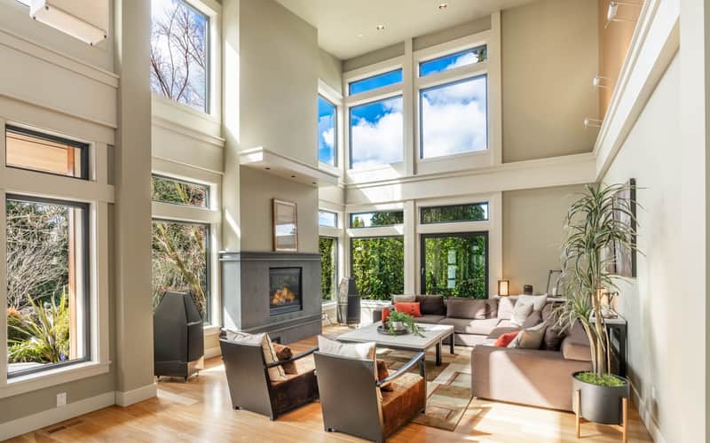 Sunlit living room with tall windows, a stone fireplace, and warm wood floors
