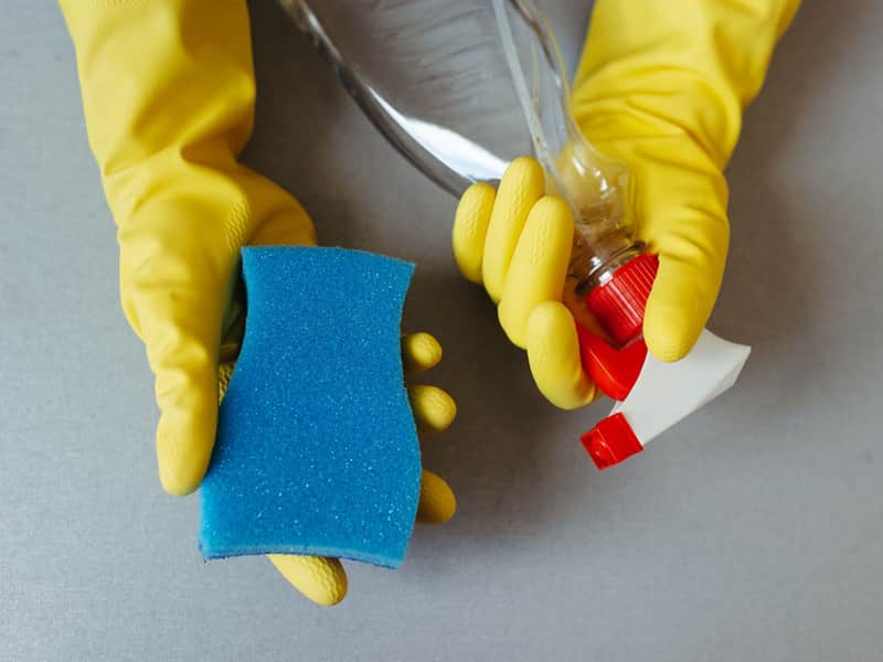 Manos con guantes de goma amarillos sosteniendo una esponja y una botella de spray