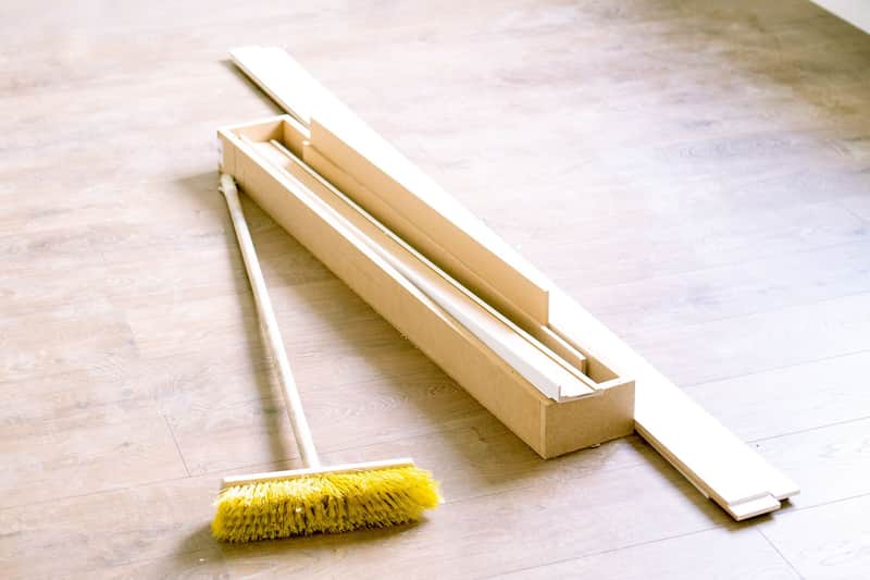 Escoba y molduras sobre el piso desnudo de una habitación recién renovada