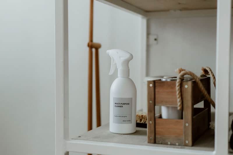 Botella de spray y caja de madera con productos de limpieza en un estante blanco