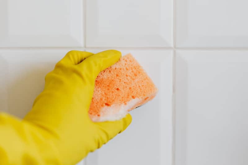 Scrubbing wall tile with a sponge during a deep clean